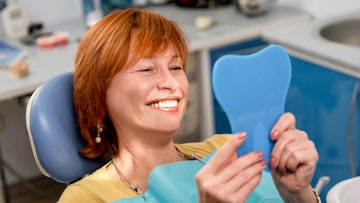 Woman in dental chair looking at her dental implants in a mirror