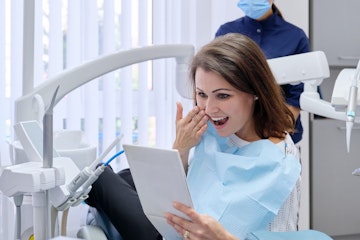 Woman in dental chair smiling looking into mirror at her new dental implants